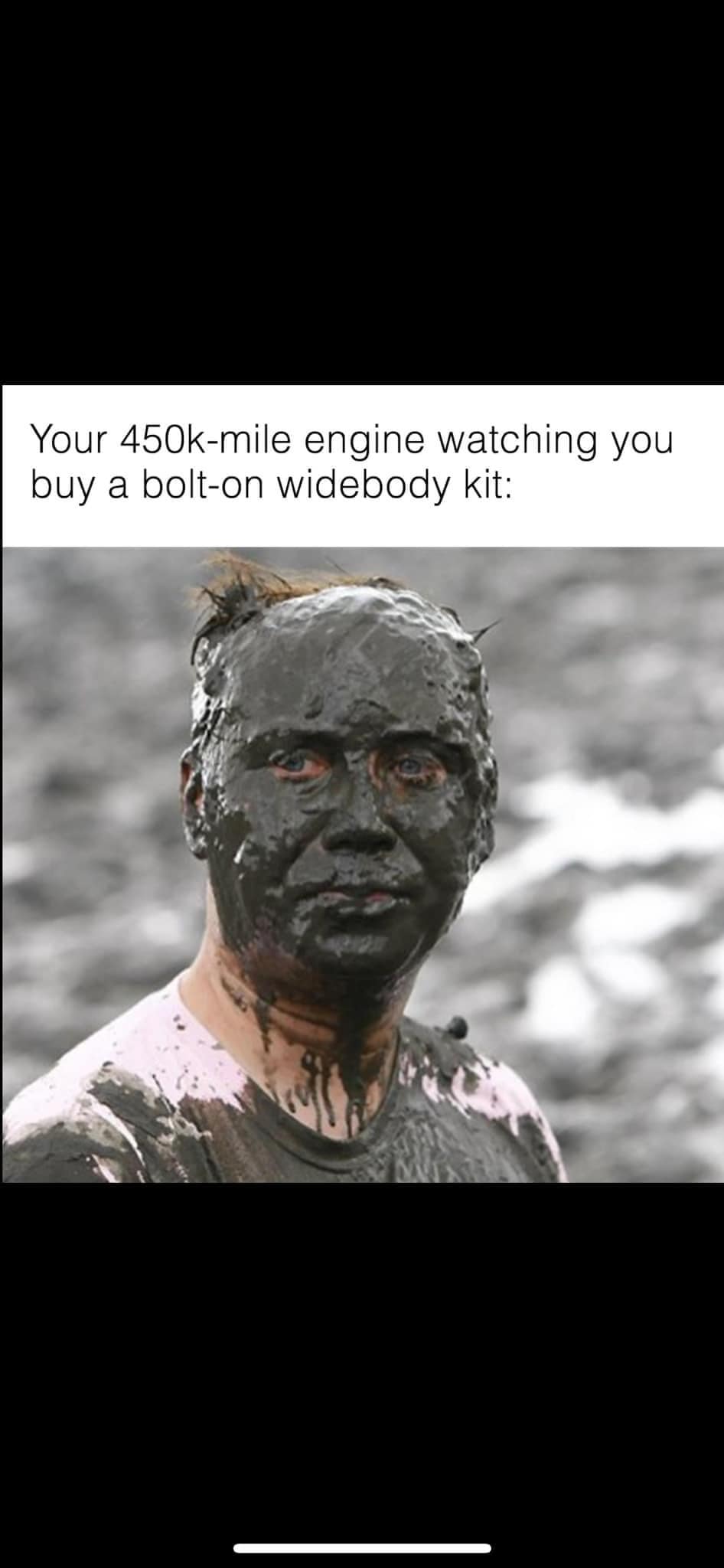 The meme is a humorous comparison between a 450k-mile engine and a person who has been covered in a thick, dirty, and possibly even hazardous substance. The image shows a person covered in a dark, oily, and potentially toxic substance, with a look of disgust and discomfort. The text above the image reads: "Your 450k-mile engine watching you buy a bolt-on widebody kit:".